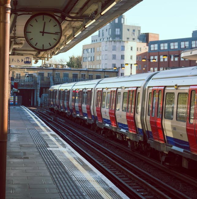 A view of multiple modern passenger trains with yellow and black accents parked on railway tracks near Earls Court station in London. The trains are aligned in parallel lines, with some facing towards the camera and others pointing away, situated on a busy railway yard. Overhead electrical wires and poles run above the tracks, which are surrounded by a mix of urban infrastructure including fencing, small buildings, and residential or commercial structures in the background. The sky is overcast, and the scene appears to be during daytime with diffuse natural light. This setting reflects the context of home relocation and moving logistics, as the railway yard is associated with transporting goods or furniture during a house move. Occasionally, Removal Van Earls Court may utilize such transport infrastructure for efficient furniture transport and logistics management during house removals near Earls Court station.